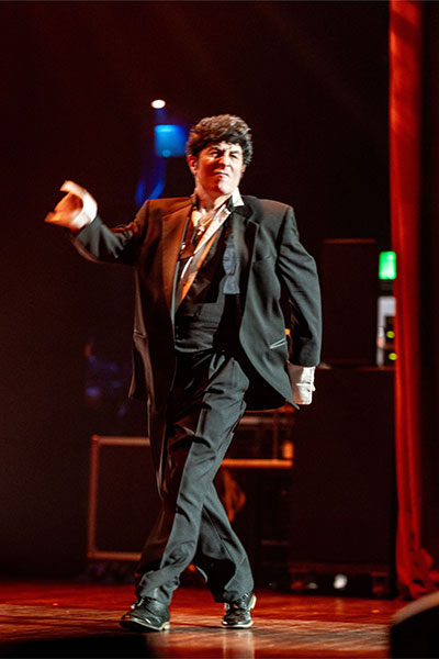 Mott, Motown and More event photo of a man dressed in a black tuxedo with the bow tie undone dance walking across the stage