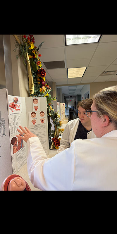 Two women discussing in front of tri-folded presentation board