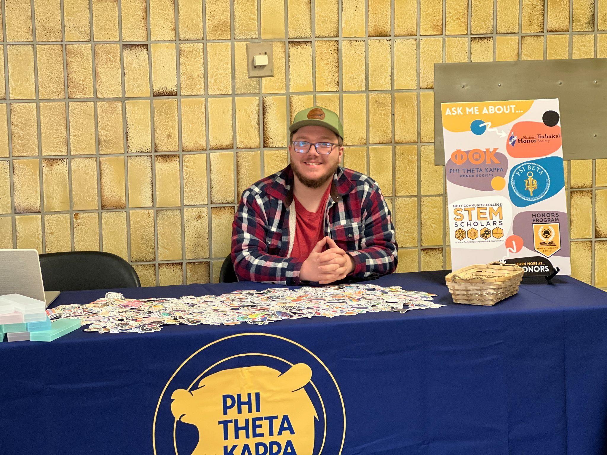 Student sitting behind a PTK information table in Curtice-Mott Complex